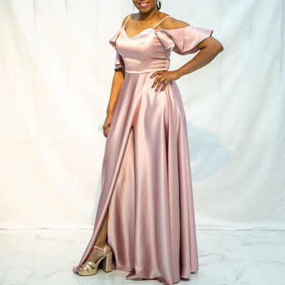 Vestido longo rosa acetinado com decote ombro a ombro e fenda, mulher posando em fundo branco