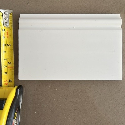 Rodapé branco com corte decorativo e fita métrica amarela a medir.