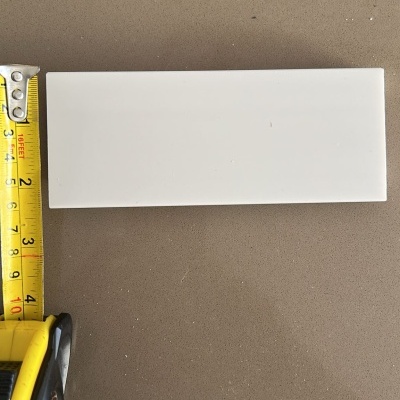 Azulejo branco retangular com fita métrica amarela ao lado sobre superfície castanha