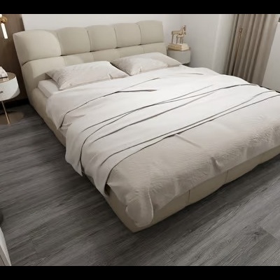 Cama estofada bege com cabeceira acolchoada, manta riscada e candeeiros brancos em quarto