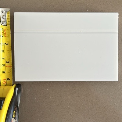 Azulejo cerâmico branco retangular com linha horizontal em relevo e fita métrica amarela ao lado