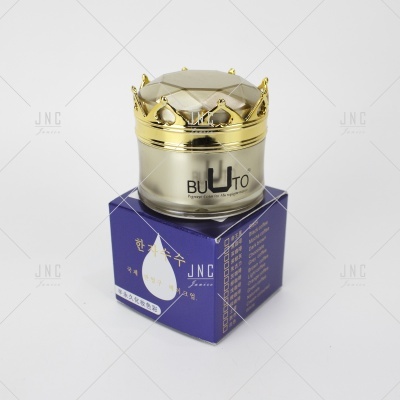 Frasco de creme facial com tampa dourada em formato de coroa sobre caixa azul com texto em coreano