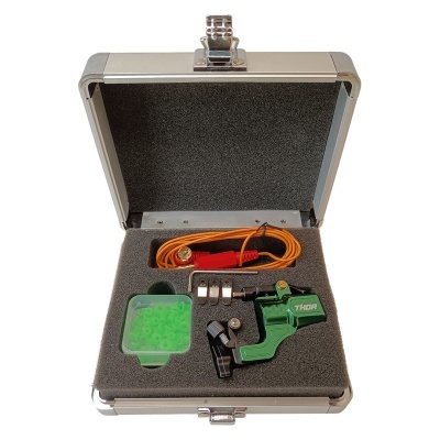 Mala metálica prateada aberta com dispositivo verde, recipiente com bolinhas verdes, peças metálicas e cabo laranja