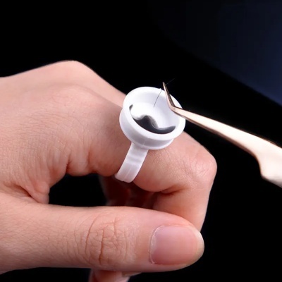 Anel branco com cola preta e pinça dourada numa mão