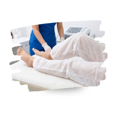 Pessoa deitada com calças brancas enquanto profissional de saúde em uniforme azul usa luvas em consultório