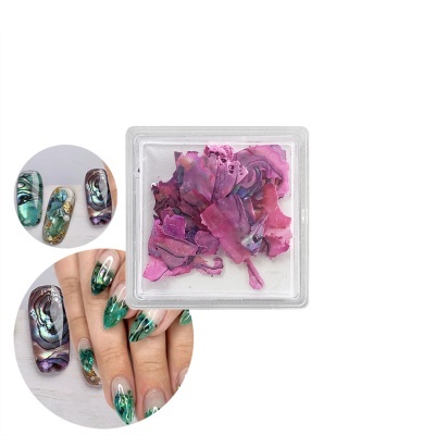 Unhas artificiais com padrão marmoreado verde e roxo e pétalas secas cor de rosa em recipiente transparente