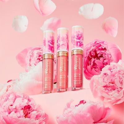 Três batons líquidos Eveline Cosmetics com tampa floral e flores cor de rosa ao redor