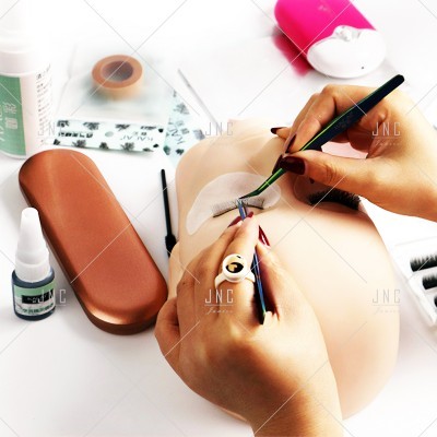 Aplicação de extensões de pestanas em cabeça de treino com ferramentas e produtos de beleza ao redor