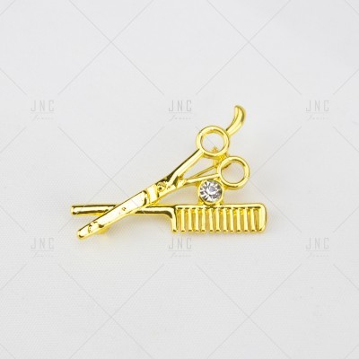 Broche dourado tesoura e pente com cristal sobre fundo branco