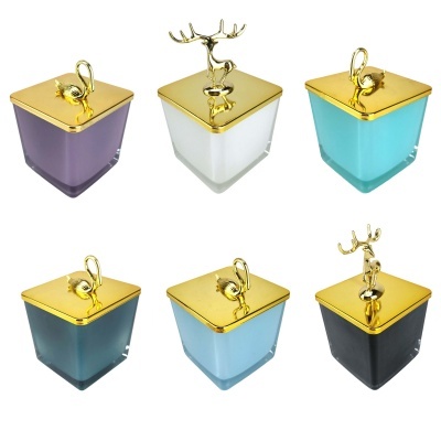 Seis velas em recipientes de vidro coloridos com tampas douradas e figuras decorativas douradas