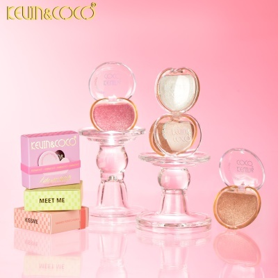 Sombras de olhos KEVIN&COCO em embalagem transparente com cores rosa, branco e dourado em suportes de vidro com fundo rosa