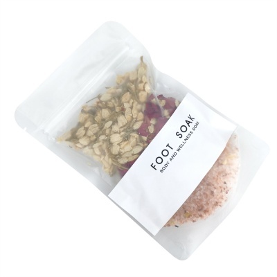 Pacote transparente com sais rosa e pétalas secas, etiqueta 'FOOT SOAK BODY AND WELLNESS SOAP'