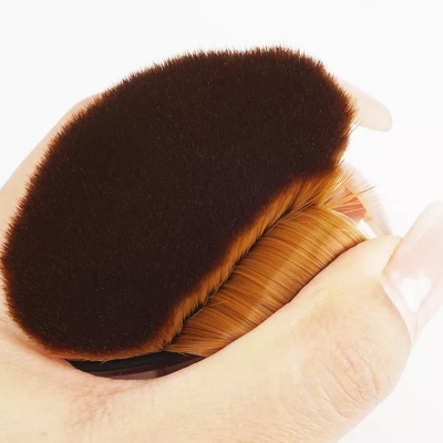 Pincel de maquilhagem compacto com cerdas castanhas e cabo preto segurado por dedos