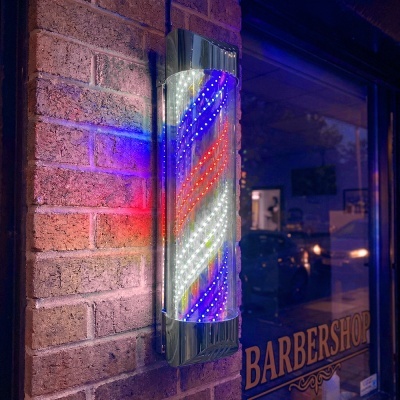 Letreiro luminoso LED de barbearia em parede de tijolos junto a porta de vidro com letreiro BARBERSHOP