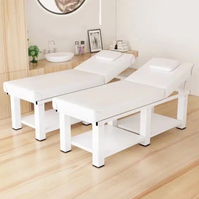 Duas camas de massagem brancas lado a lado em ambiente com piso claro de madeira e bancada ao fundo.