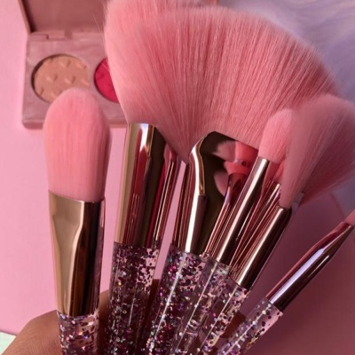 Conjunto de pincéis de maquilhagem cor-de-rosa com glitter e paleta ao fundo