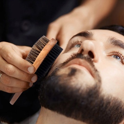 Escova para barba com cerdas naturais e sintéticas em mão masculina a pentear barba