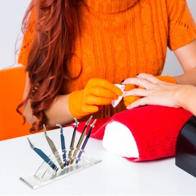 Manicure a tratar unhas com luvas laranja, ferramentas de manicure e toalha vermelha