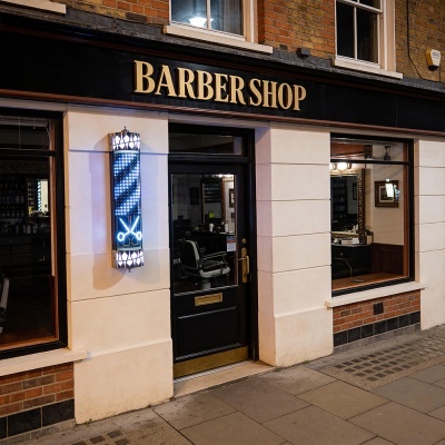 Fachada de barbearia com letreiro BARBERSHOP e sinal luminoso azul e branco com tesouras