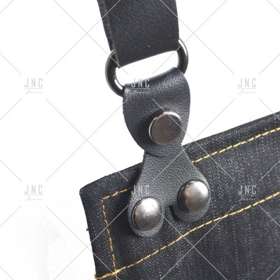 Detalhe de avental preto com alça de pele sintética e botões metálicos