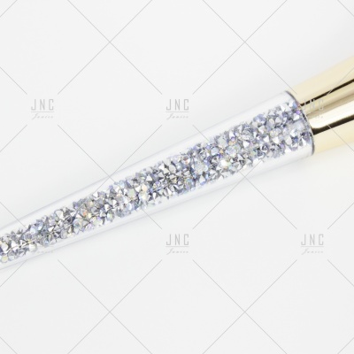 Aplicador de maquilhagem com cristais prateados no cabo e tampa dourada.