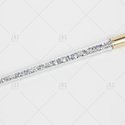 Objeto tubular transparente com pedras brilhantes prateadas e extremidade dourada