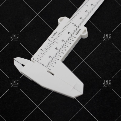 Paquímetro branco em plástico com escala métrica preto sobre fundo preto.