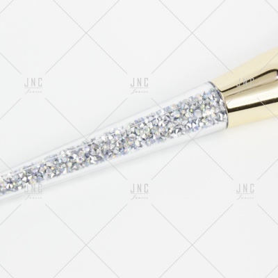 Escova de maquilhagem com cabo transparente e punho dourado.