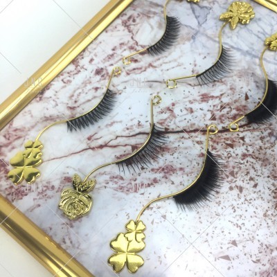 Peças de arte com cílios postiços e detalhes dourados de trevo e abacaxi numa moldura dourada.