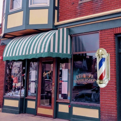 Fachada de barbearia com toldo verde e branco e coluna luminosa clássica