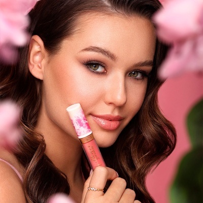 Mulher segurando batom líquido rosa com tampa branca floral