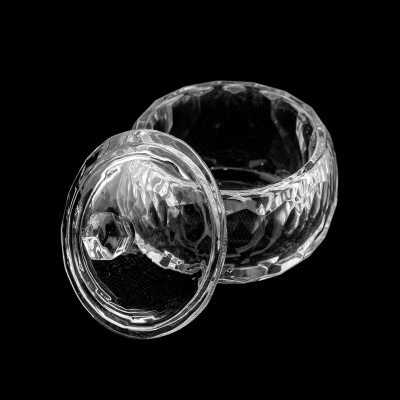 Pote redondo transparente de vidro com tampa sobre fundo preto