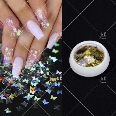 Unhas com verniz rosa claro e glitter em forma borboletas holográficas e recipiente com confetes dourados