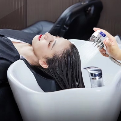 Mulher a lavar cabelo numa cadeira com lavatório branco e chuveiro manual