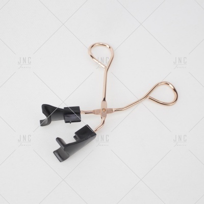 Curvador de pestanas metálico dourado com apoios pretos sobre fundo branco