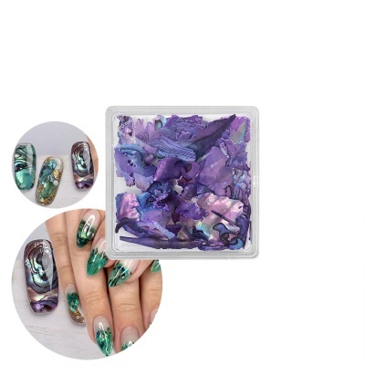 Folhas decorativas de unhas roxas com padrão marmoreado em caixa transparente junto a unhas decoradas nas cores verde, azul e roxo