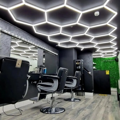 Sala de salão com cadeiras pretas, espelhos e teto iluminado em padrão hexagonal