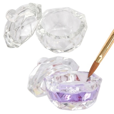 Duas pequenas caixas faceteadas de vidro com tampas, uma com líquido lilás e pincel dourado, sobre fundo branco.