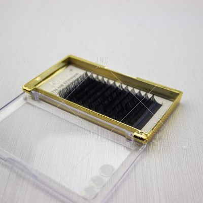 Estojo dourado com pestanas falsas pretas e tampa transparente aberta sobre fundo branco