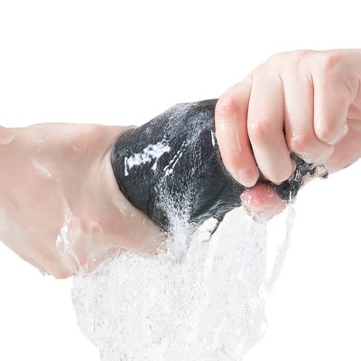 Mão a espremer objeto negro com água a sair