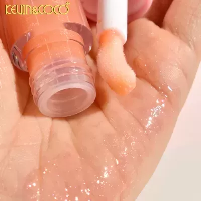 Batom líquido alaranjado com brilho em mão, aplicador branco e embalagem rosa transparente com texto KEVIN&COCO.