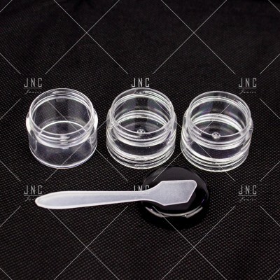 Três frascos transparentes pequenos com tampa e uma espátula branca sobre fundo preto