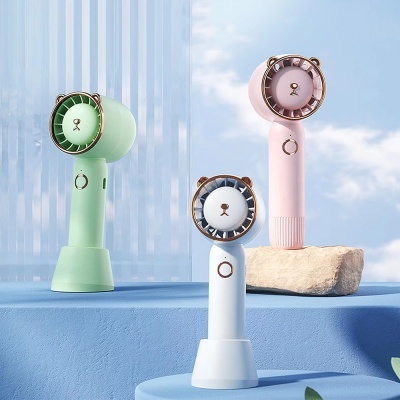 Ventiladores portáteis em forma de cabeça de urso em verde, rosa e branco sobre superfícies azuis com céu ao fundo