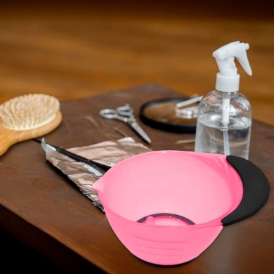 Tigela rosa com pega preta, pente de madeira, tesouras, papel alumínio e frasco spray numa mesa de madeira