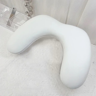 almofada branca em forma de U sobre superfície branca com caixa transparente ao lado