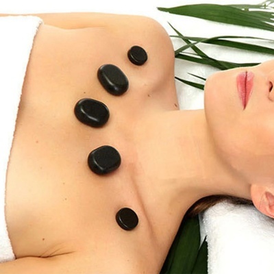 Mulher deitada com pedras pretas para massagem no peito e ombros