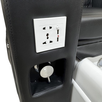 Tomada elétrica branca e regulador metálico em braço de pele preta de poltrona