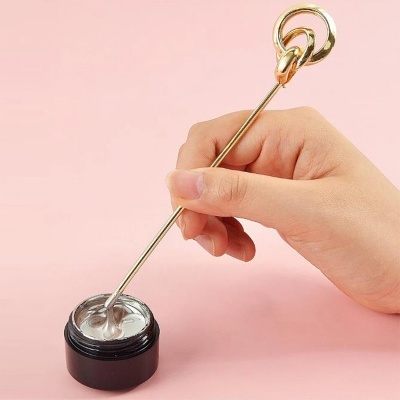 Frasco preto aberto com creme e espátula dourada a ser segurada pela mão