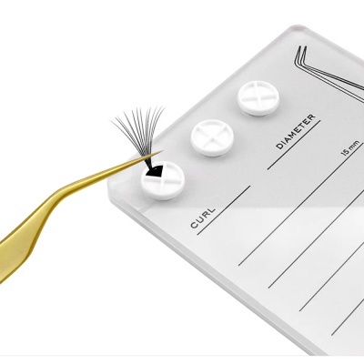 Pinça dourada a segurar conjunto de pestanas sobre cartão branco com inscrições e inserções para pestanas.