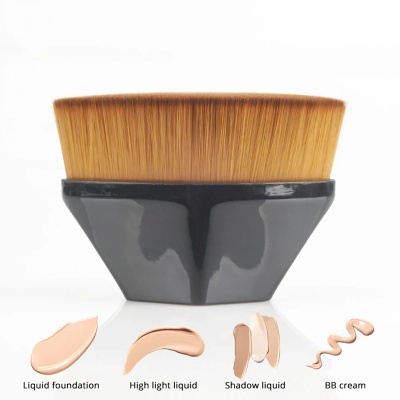 Pincel de maquilhagem com cerdas castanhas e cabo preto junto a amostras de maquilhagem líquida